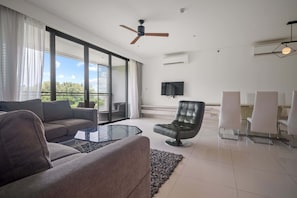 A modern living room with a sofa, armchair, glass coffee table, and a TV mounted on the wall. - Cassia Residences Building 2 in Laguna by Banyan Living (Choeng Thale)