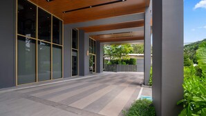 A modern building with large glass doors, a covered walkway, and a landscaped garden area. - Laguna Beachside Residences Building 4 by Banyan Living (Choeng Thale)