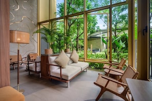 Ein modernes Interieur mit einer Couch, Sesseln und einem Tisch nahe großer Fenster mit Blick auf einen Garten.