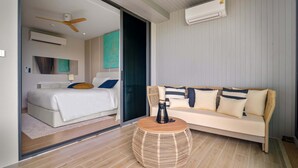 A modern hotel room with a bed, sofa, and round wicker coffee table. - Laguna Beachside Residences Building 3 by Banyan Living (Choeng Thale)