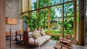 A modern interior with a sofa, chairs, and a table near large windows overlooking a garden. - Laguna Beachside Residences Building 3 by Banyan Living (Choeng Thale)