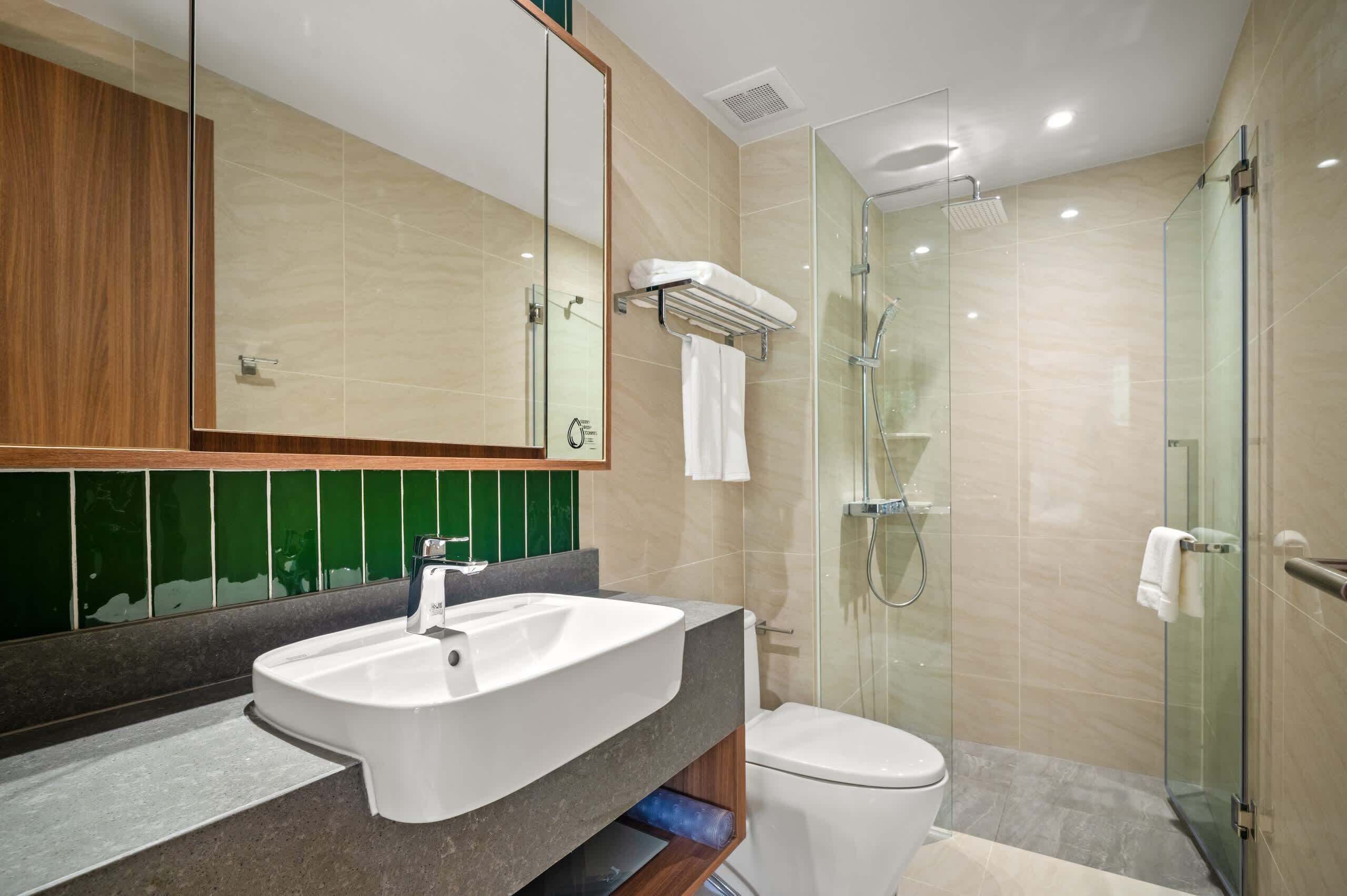 Une salle de bain moderne avec un grand miroir, un lavabo, des toilettes et une douche séparée par une paroi de verre.