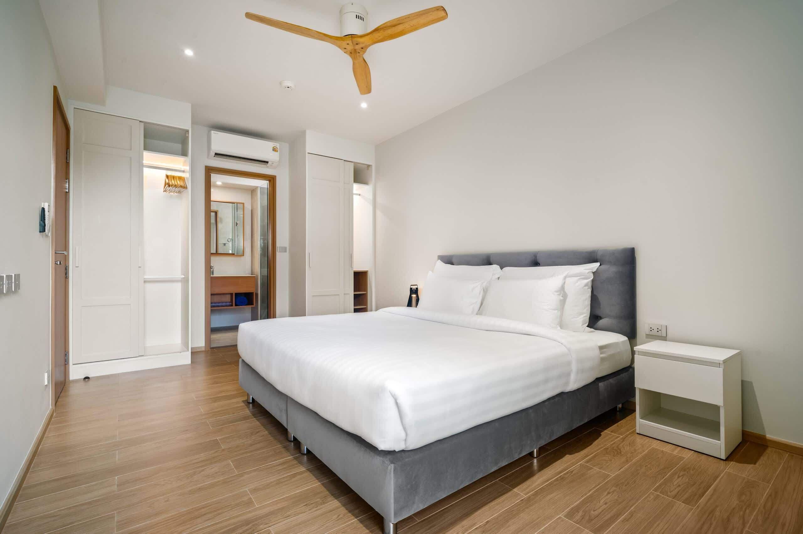 A modern bedroom with a large bed, a ceiling fan, and a white nightstand.