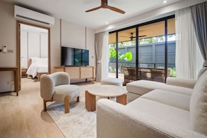 A modern living room with a sofa, armchairs, a TV, and a large window with a view. - Laguna Beachside Residences Building 2 by Banyan Living (Choeng Thale)