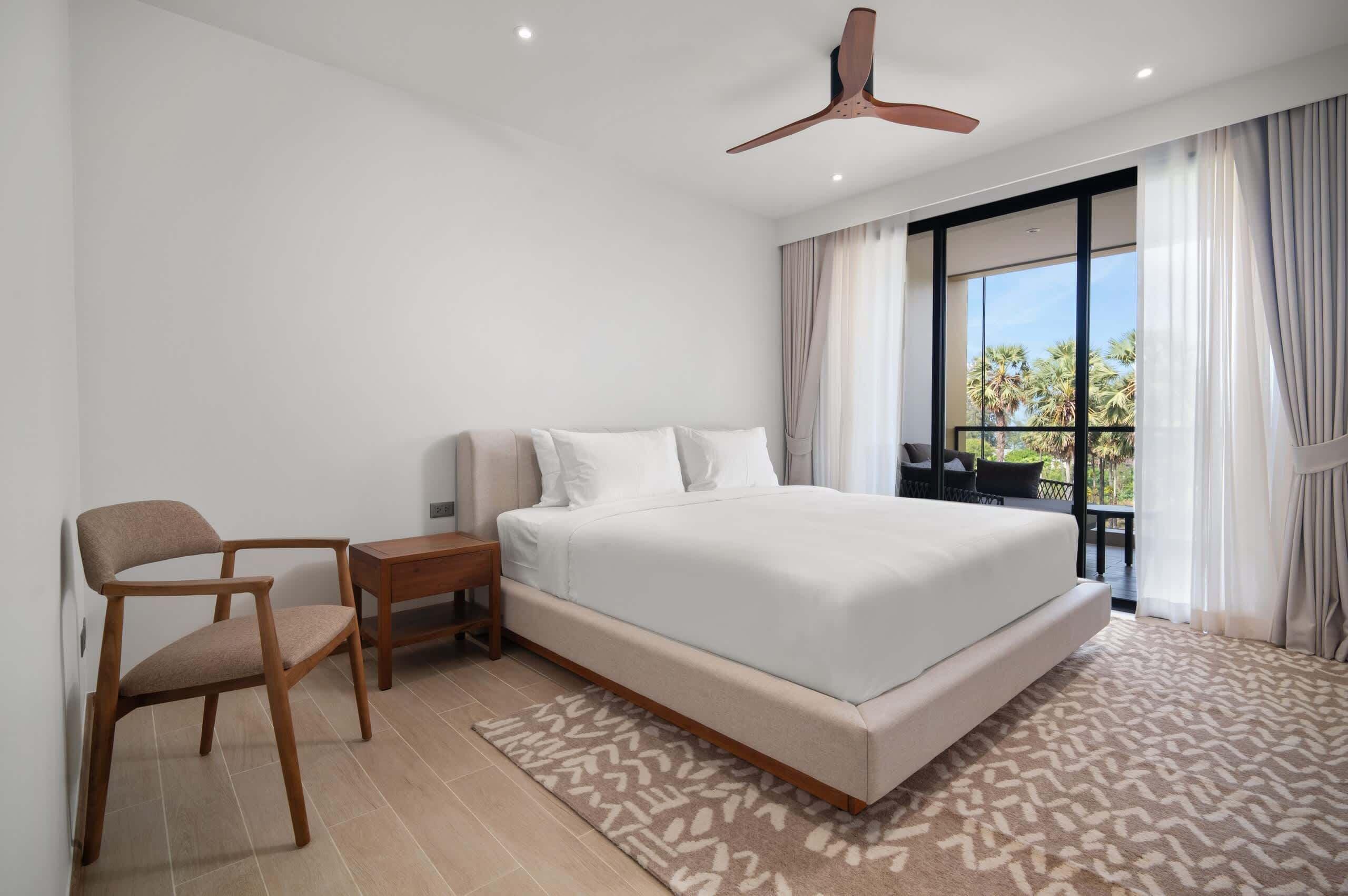A bedroom with a large bed, a chair, a nightstand, and a ceiling fan.