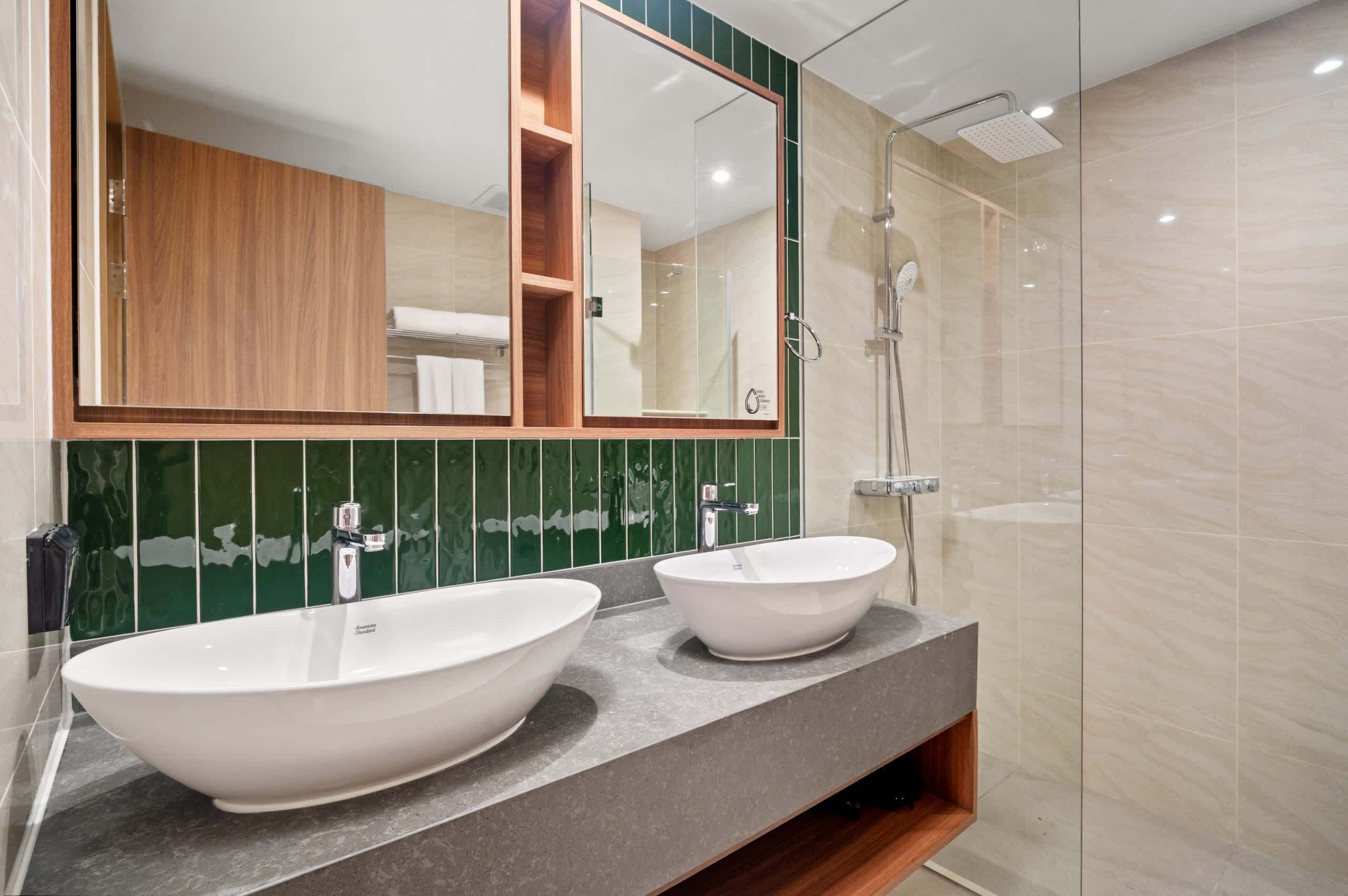 A modern bathroom with a large mirror, two vessel sinks, a shower, and a wooden cabinet.