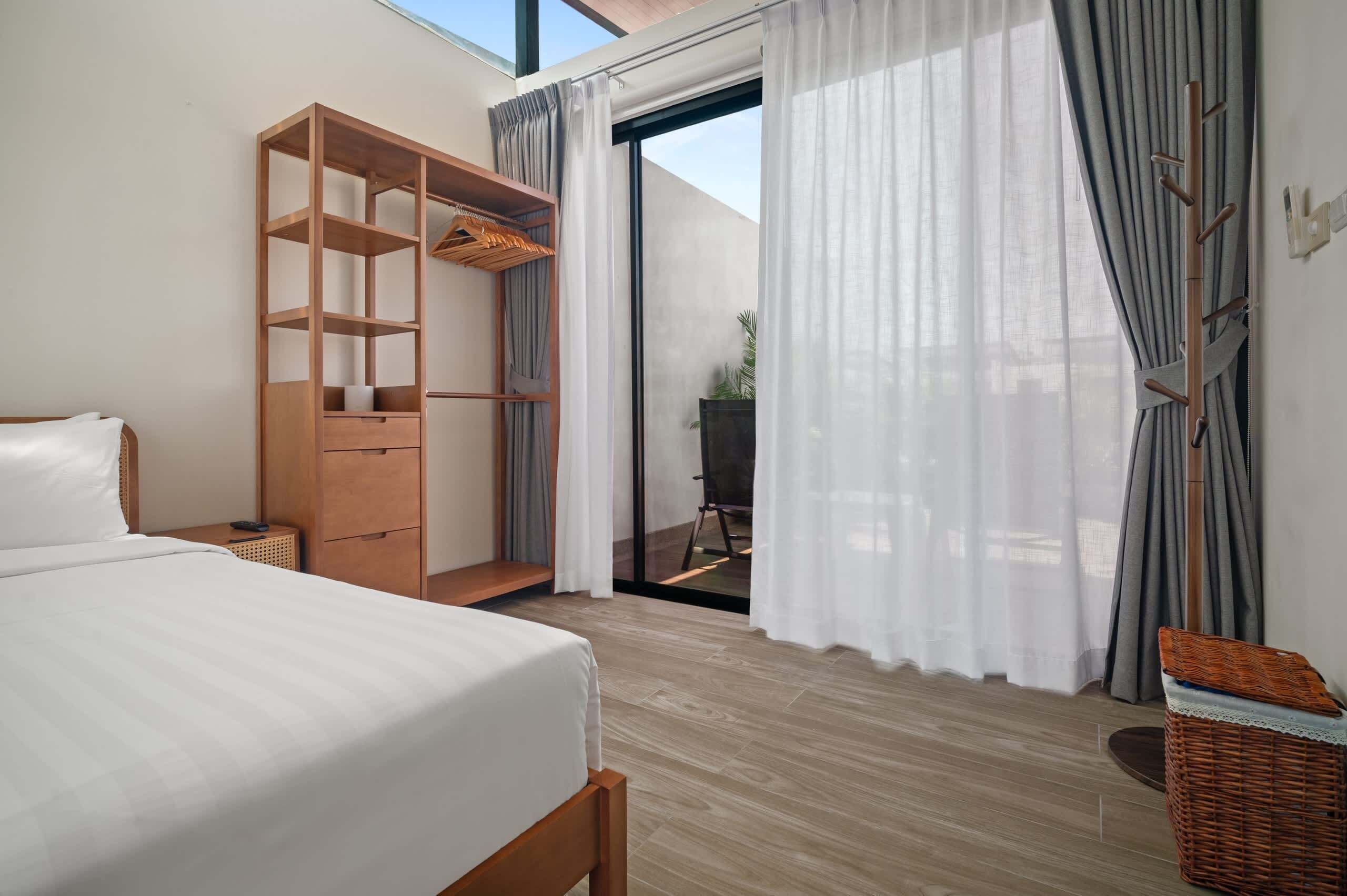 Une chambre à coucher avec un lit, une armoire en bois, un balcon avec une chaise et une vue sur l’extérieur.