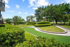 A landscaped area with a green artificial turf, neatly trimmed bushes, and trees. - Skypark Aurora in Laguna by Banyan Living (Choeng Thale)