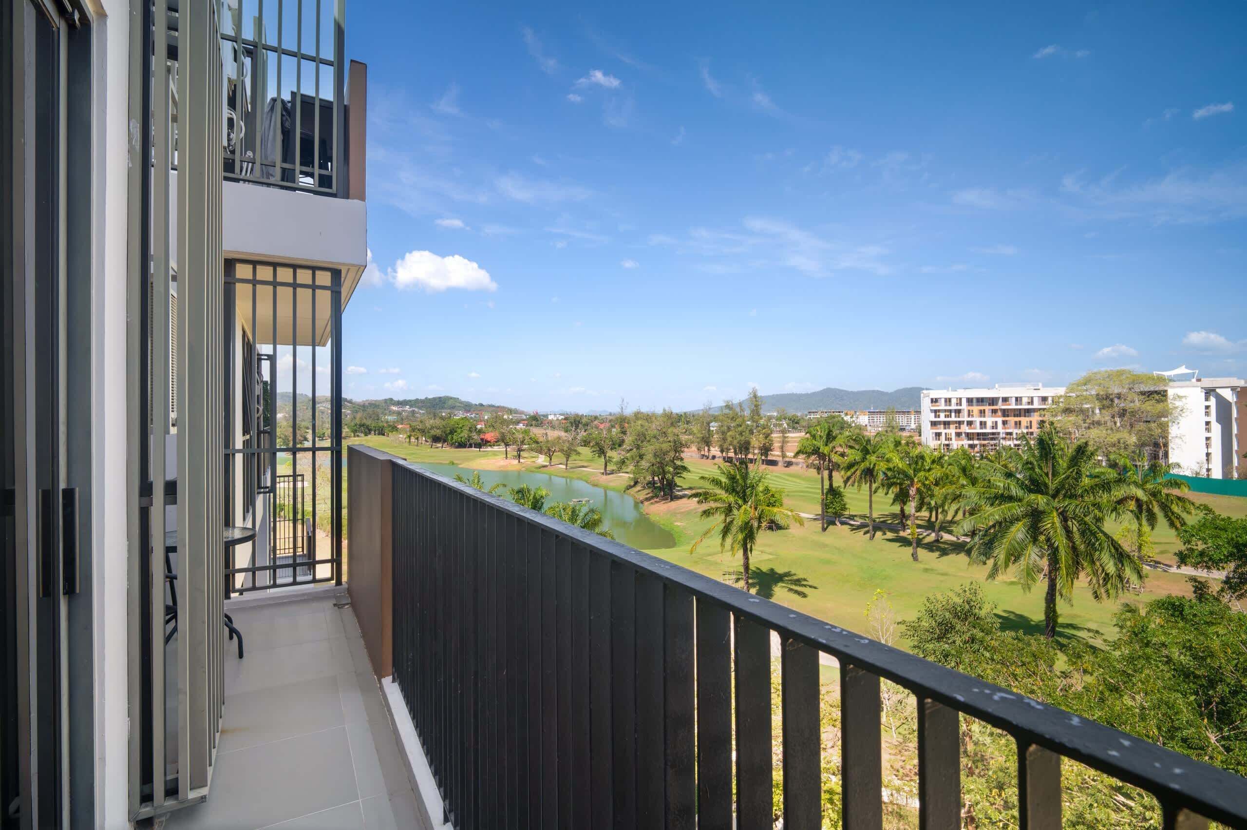Un balcón con vista a un campo de golf, palmeras y edificios al fondo.