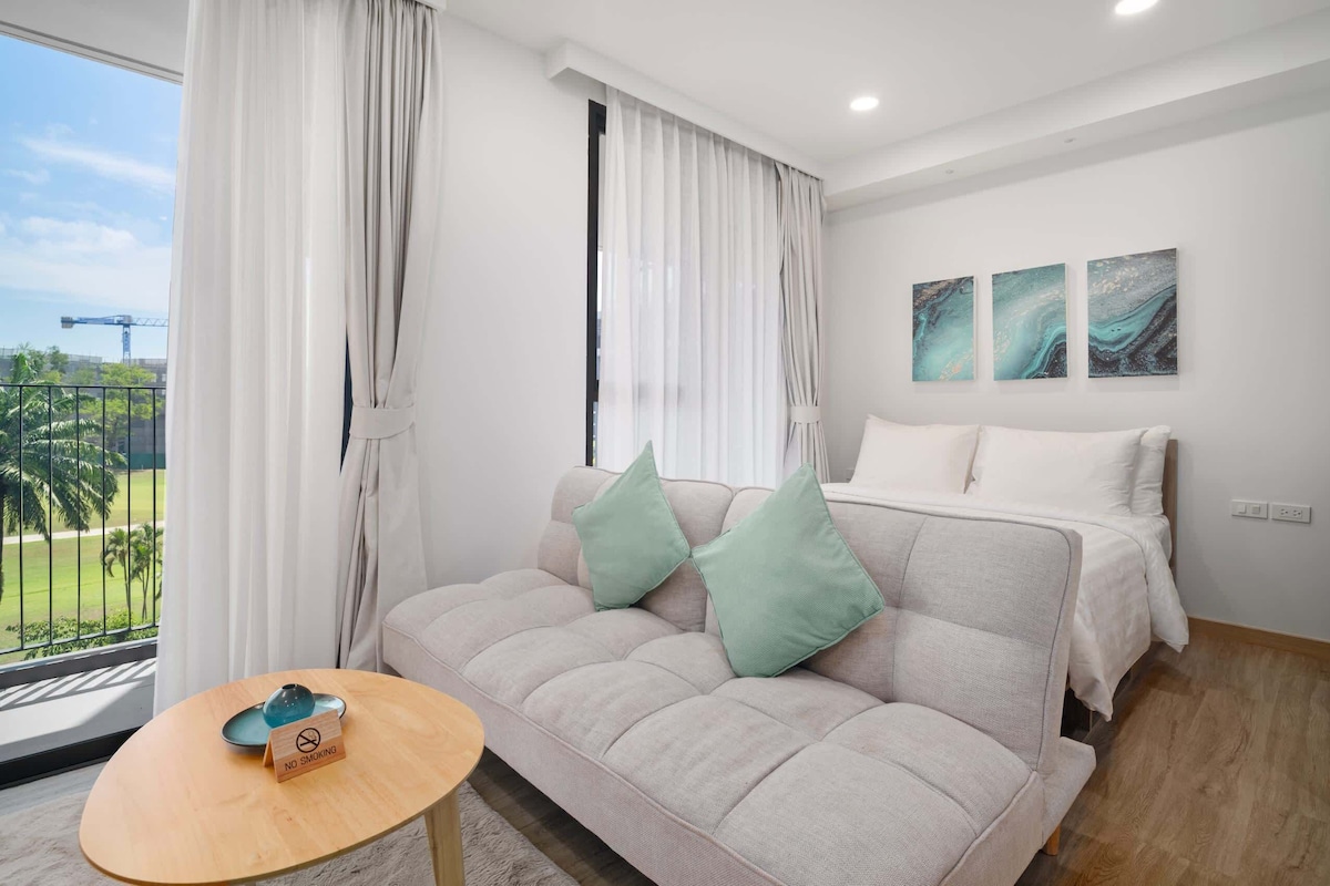 Ein modernes Hotelzimmer mit Sofa, einem kleinen Tisch, einem Bett und einem Balkon mit Blick auf Palmen und einen Baukran.