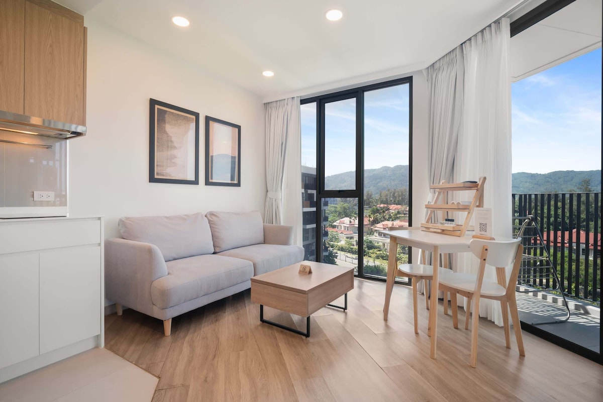 Ein modernes Wohnzimmer mit Sofa, Couchtisch und Essbereich mit Stühlen. Ein großes Fenster bietet Blick auf die Stadt und die Berge.