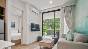 A modern hotel room with a bed, a flat-screen TV, a sofa, a coffee table, and a large window with curtains. - Skypark Aurora in Laguna by Banyan Living (Choeng Thale)