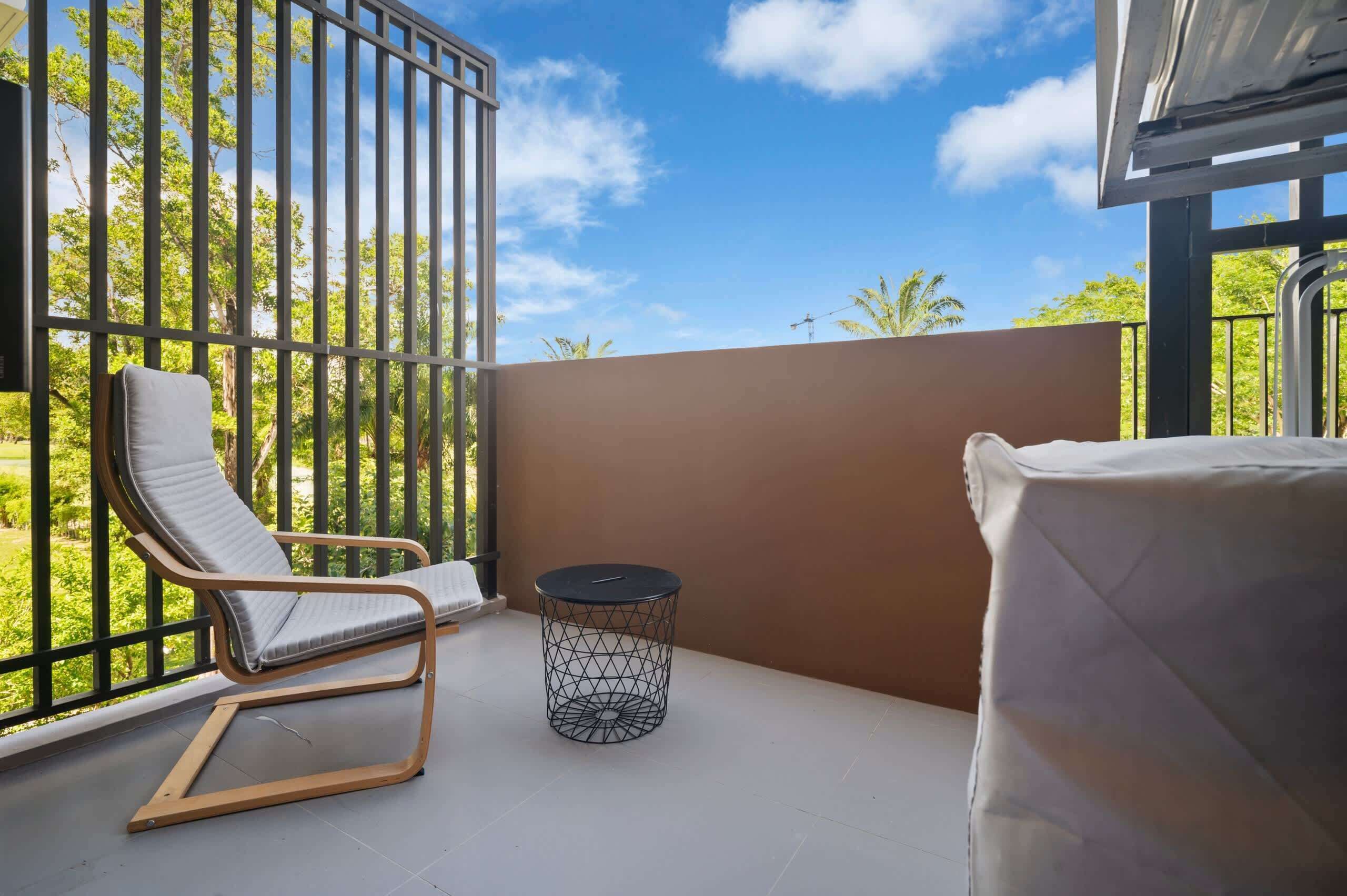 Un balcón con una silla, una mesita redonda y vistas al verdor.