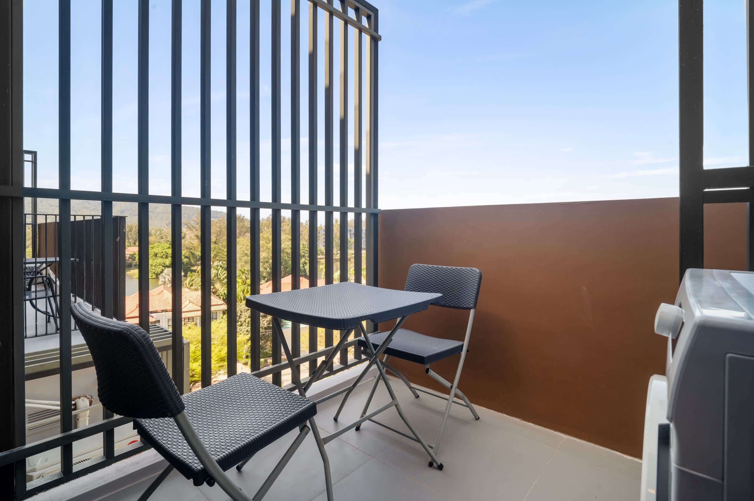 Een balkon met een tafel, twee stoelen, een barbecue en uitzicht op bomen en gebouwen.