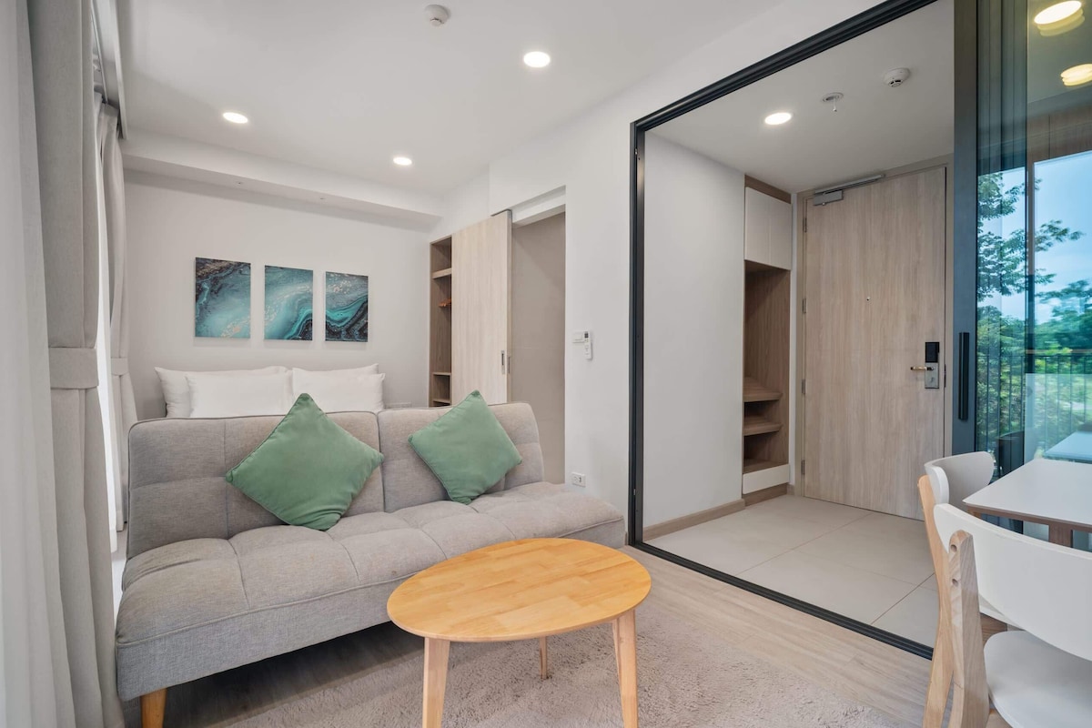 A modern living room with a sofa, a round wooden table, and a glass door leading to a balcony.