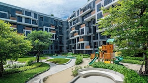 Un immeuble d’appartements moderne doté d’un terrain de jeux, d’un jardin aménagé et d’un chemin sinueux.
