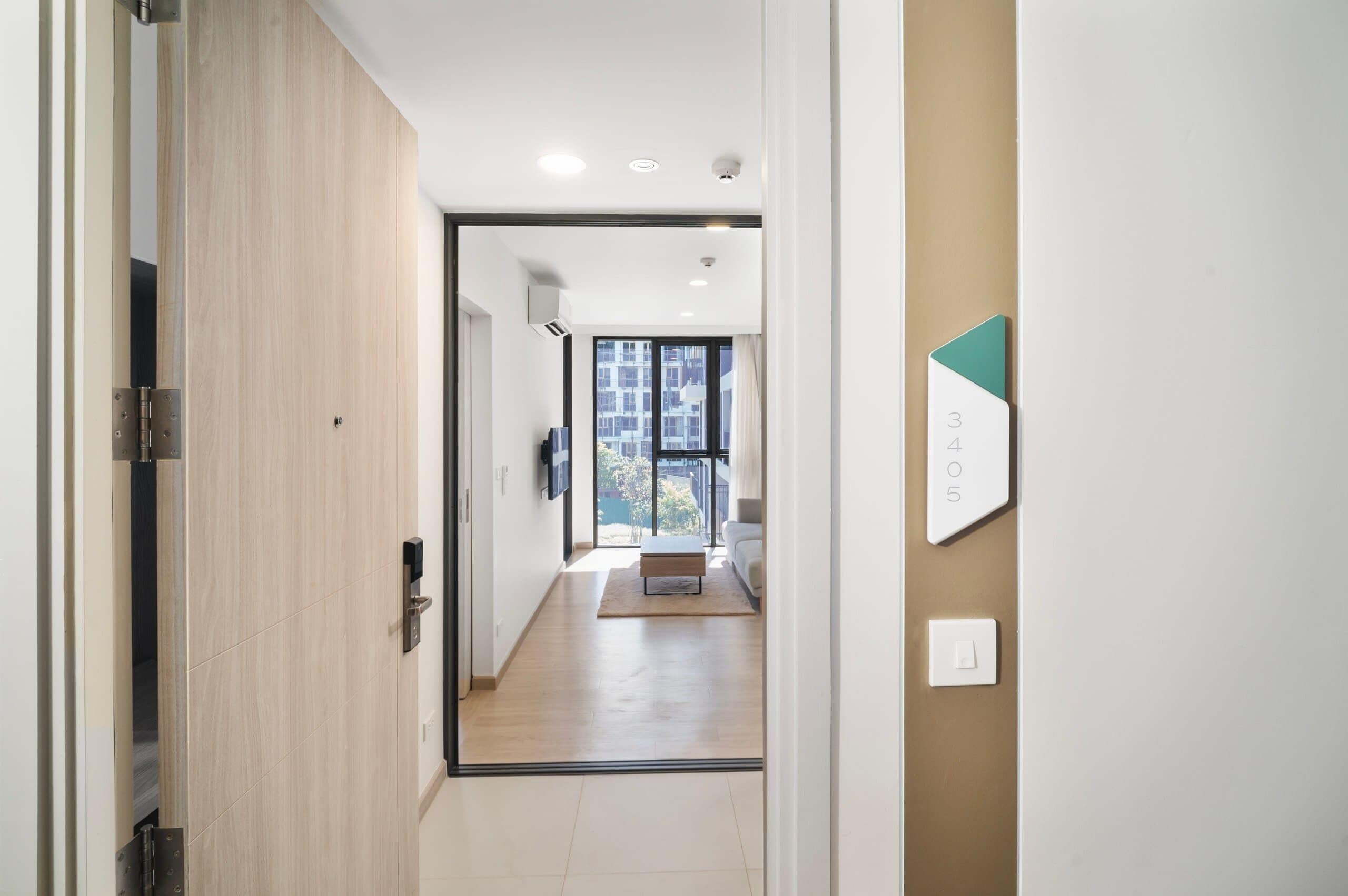 A hallway with a wooden door, a light switch, and a number sign on the wall.