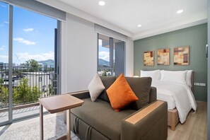 Une chambre d’hôtel moderne avec une grande fenêtre, un canapé, un lit et des œuvres d’art accrochées au mur.