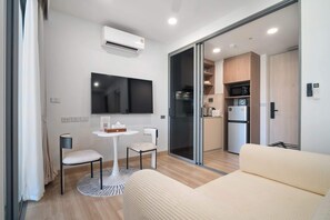 Une chambre moderne équipée d’un téléviseur à écran plat, d’une petite table avec des chaises, d’un canapé, d’une porte-fenêtre coulissante donnant sur une cuisine et d’un appareil de climatisation.
