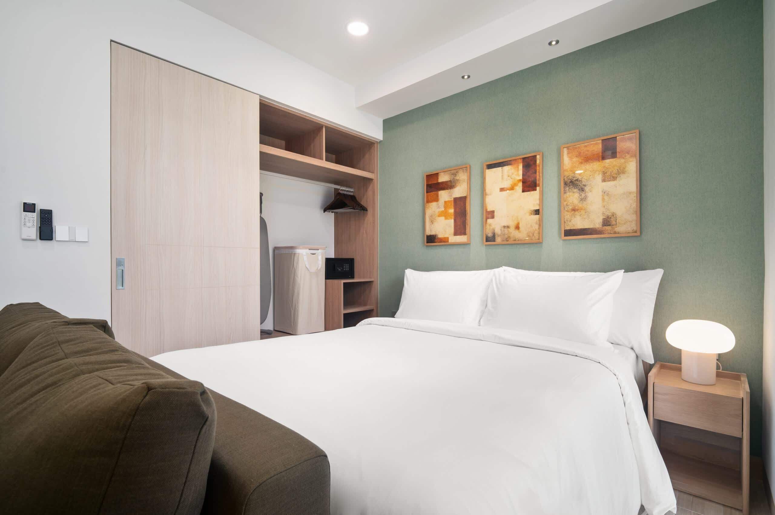 Una habitación de hotel con cama, armario, mesita de noche con lámpara y arte abstracto en la pared.