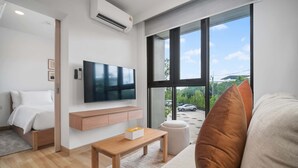 Ett modernt hotellrum med en säng, en tv som är monterad på väggen, ett träbord och ett stort fönster med utsikt över omgivningen.
