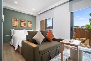 A modern room with a bed, sofa, and table, large windows, and artwork on the wall. - Skypark Celeste Building 5 in Laguna by Banyan Living (Choeng Thale)