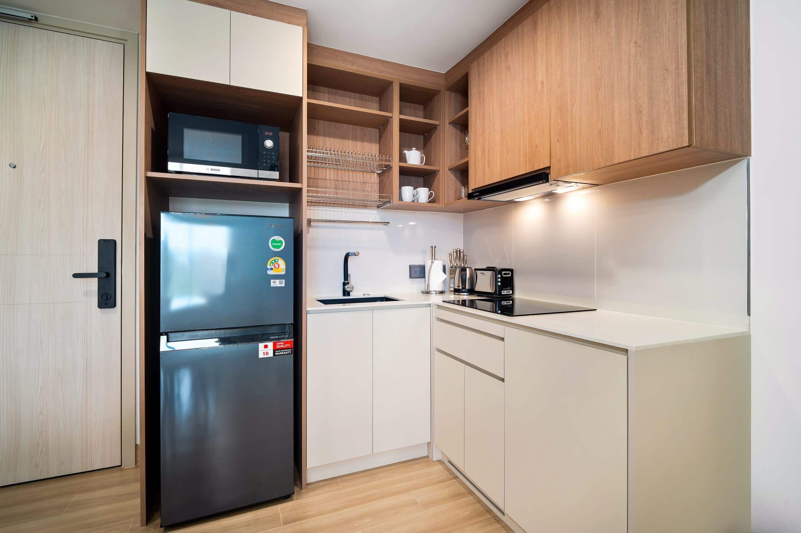 Cocina compacta con microondas integrado, refrigerador de acero inoxidable, pileta y muebles de madera.