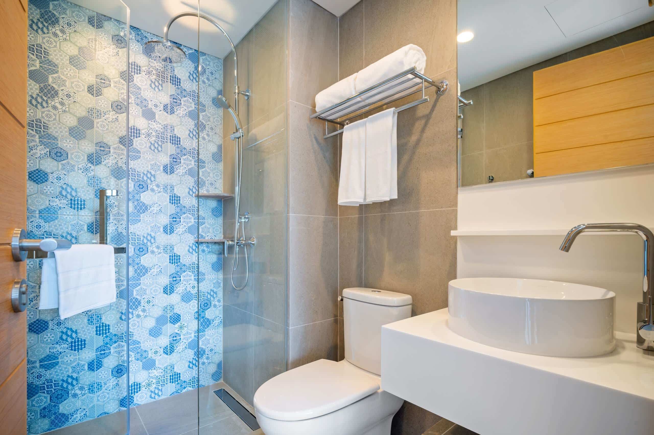 A modern bathroom with a glass shower enclosure, a white toilet, and a round sink with a mirror above.