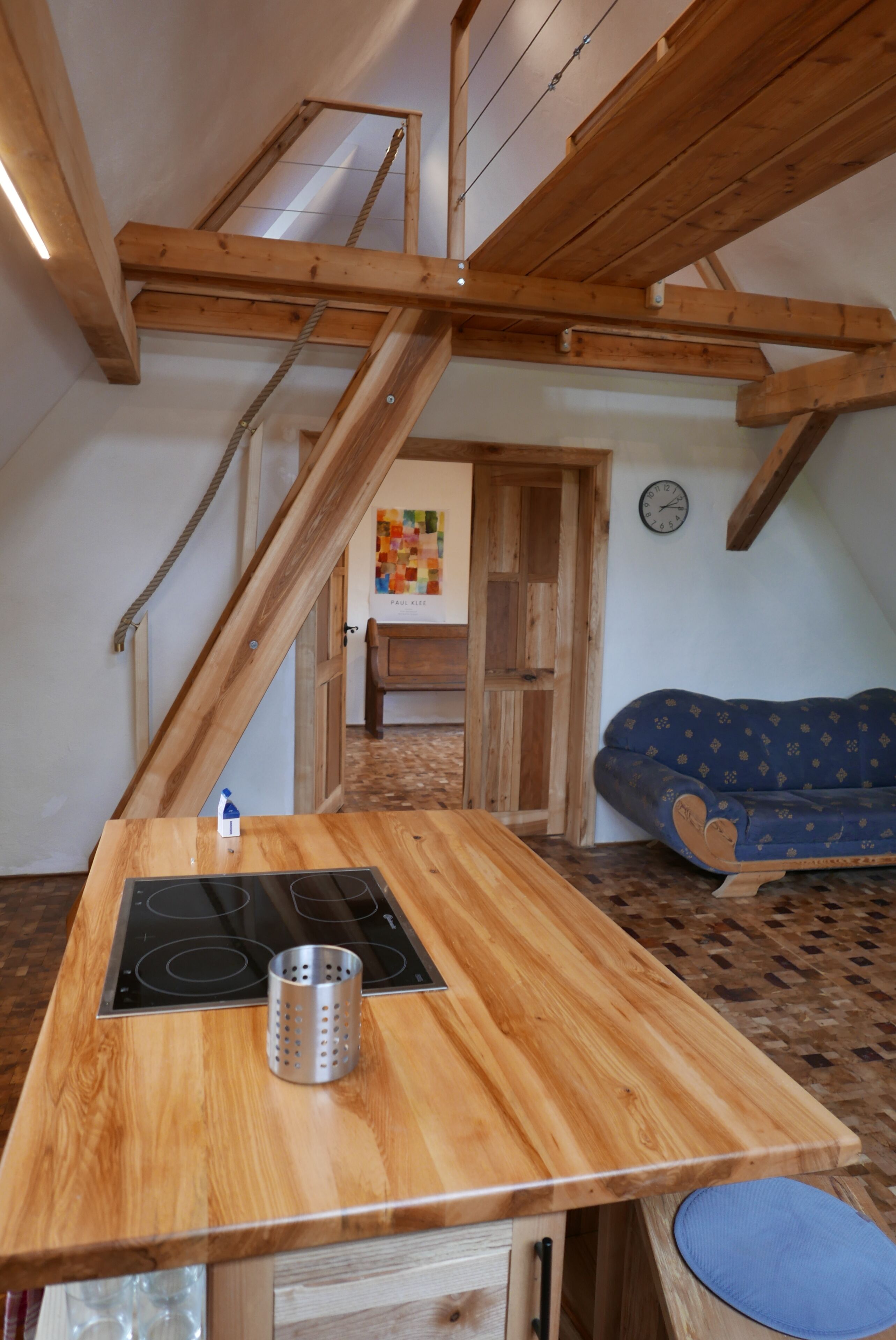 A wooden kitchen with a built-in stove, a hanging pot rack, and a blue couch in the background.