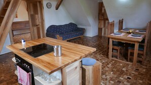 A kitchen with a wooden countertop, stove, and sink. There is a dining table with chairs and a blue sofa in the background. - Maison des Vergers, nature meets craftsmanship (Hoffen)