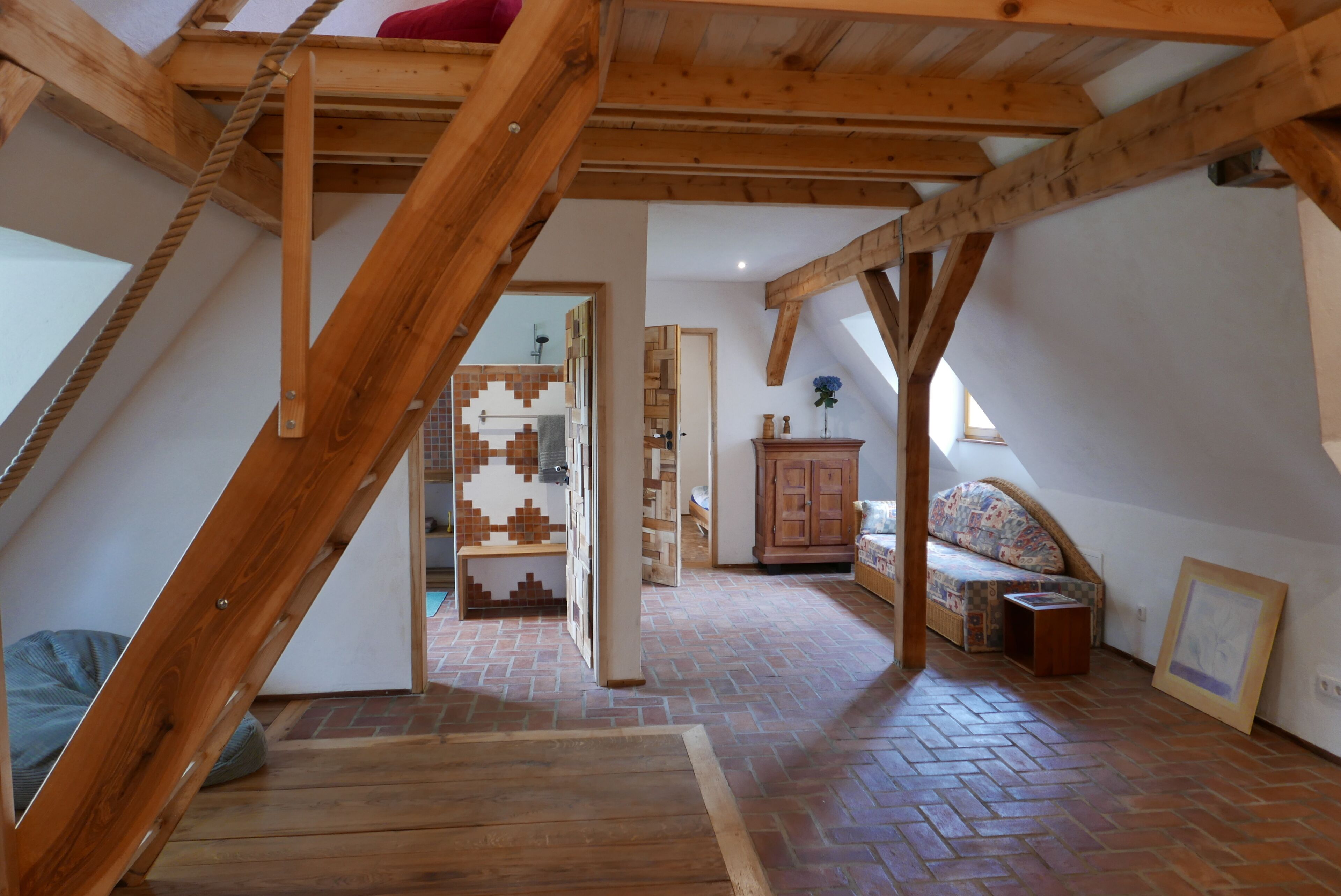 Een zolderkamer met houten balken, een visgraatvloer, een hoogslaper, een bank en een kast.