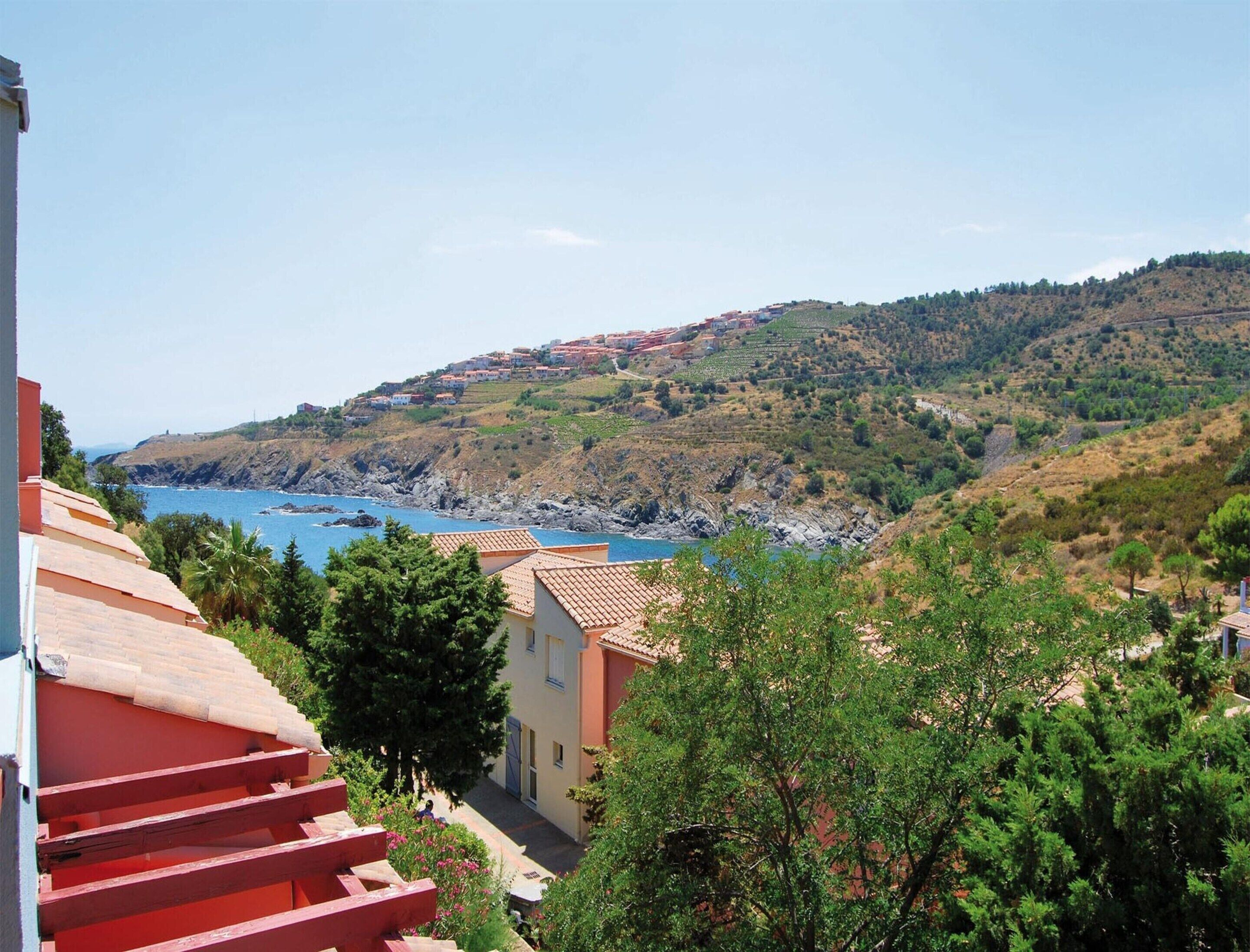 Une ville côtière avec des maisons à étages, une mer d’un bleu limpide et une colline verdoyante.