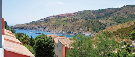 Une ville côtière avec des maisons à étages, une mer d’un bleu limpide et une colline verdoyante.