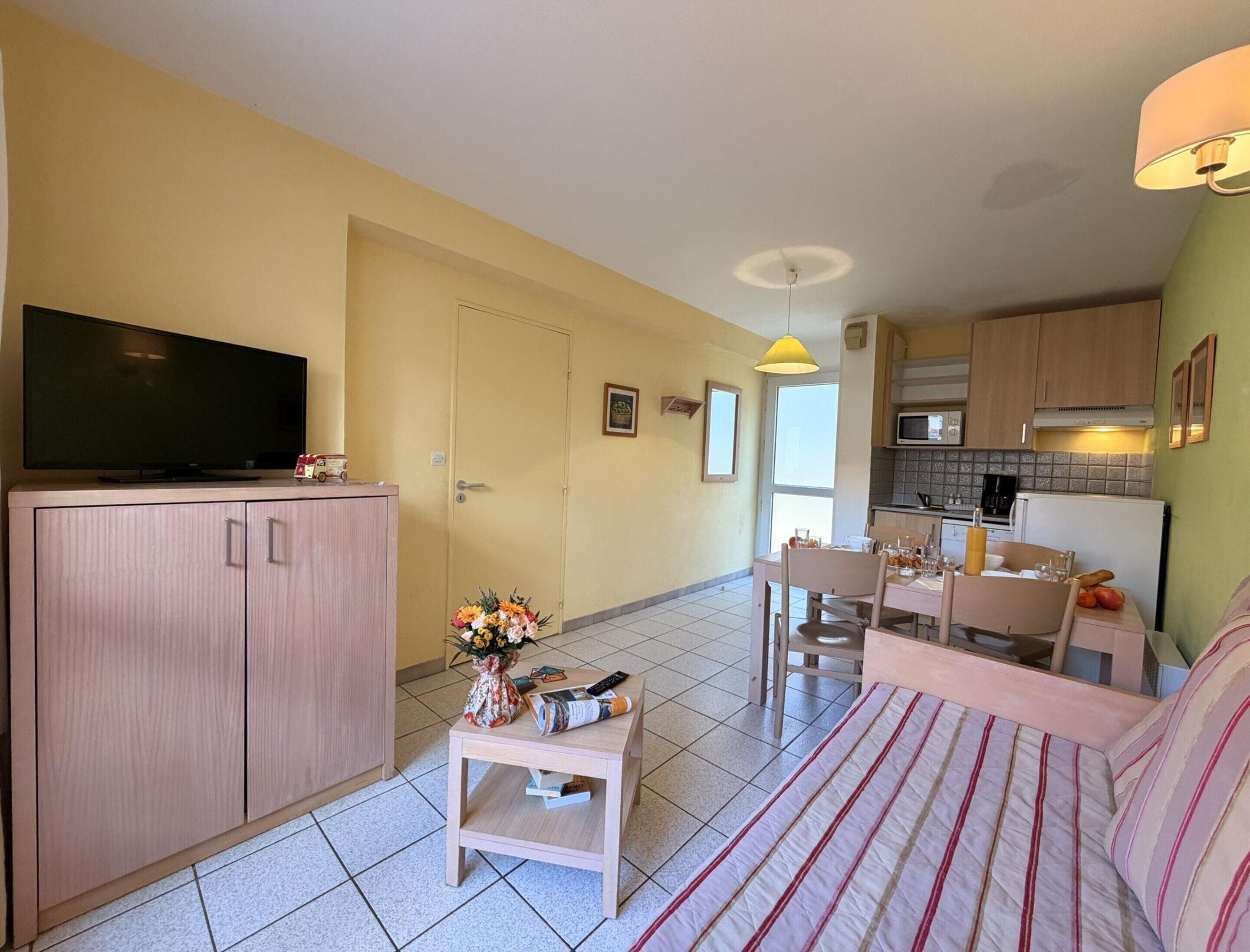 A living room with a TV, a sofa, a dining table, and a kitchen area with cabinets and a microwave.
