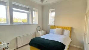 A bedroom with a bed, a bedside table, a radiator, and a window. - Bunker Golf Cottage (Prestwick)