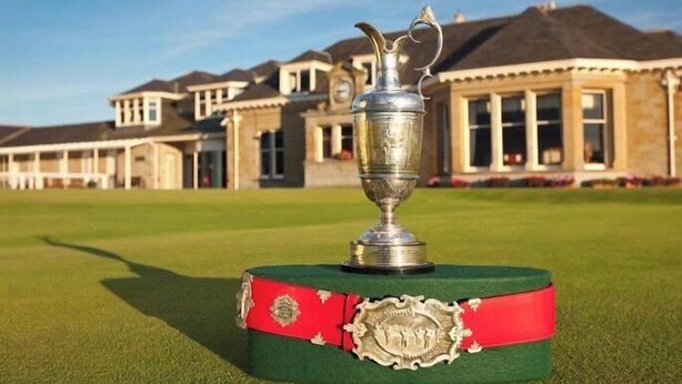 A trophy on a green base with a red band, set on a golf course with a building in the background. - Bunker Golf Cottage (Prestwick)