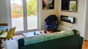 A living room with a green sofa, a dining table with chairs, a TV, and a chandelier. - Bunker Golf Cottage (Prestwick)