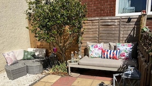 A patio with a cushioned seating area, a small table with a drink, and a lantern. - Bunker Golf Cottage (Prestwick)