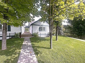 A residential area with a pathway leading to a house with a gabled roof and a front porch. - The Chief's Landing- Lower Level Condo (Bellaire)