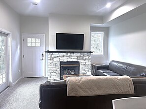 A living room with a stone fireplace, a black leather sofa, and a television mounted above the fireplace. - The Chief's Landing- Lower Level Condo (Bellaire)