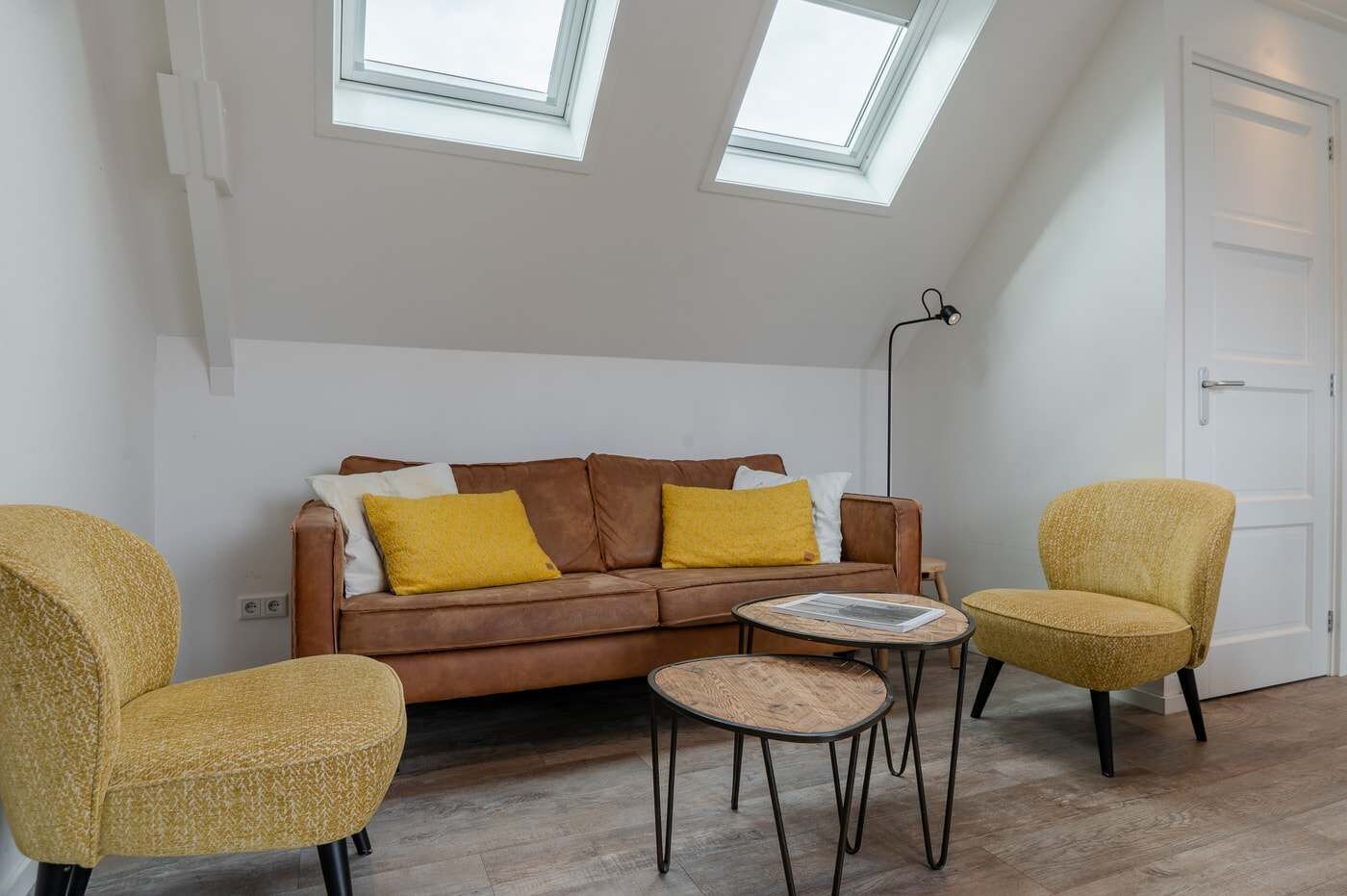 Ein Wohnzimmer mit einem braunen Sofa, zwei gelben Sesseln, einem kleinen runden Tisch und einer Stehlampe.