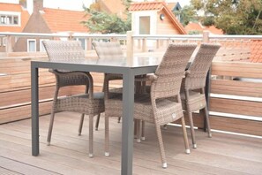 Eine Terrasse mit Tisch und Korbstühlen, umgeben von einem Holgitter.