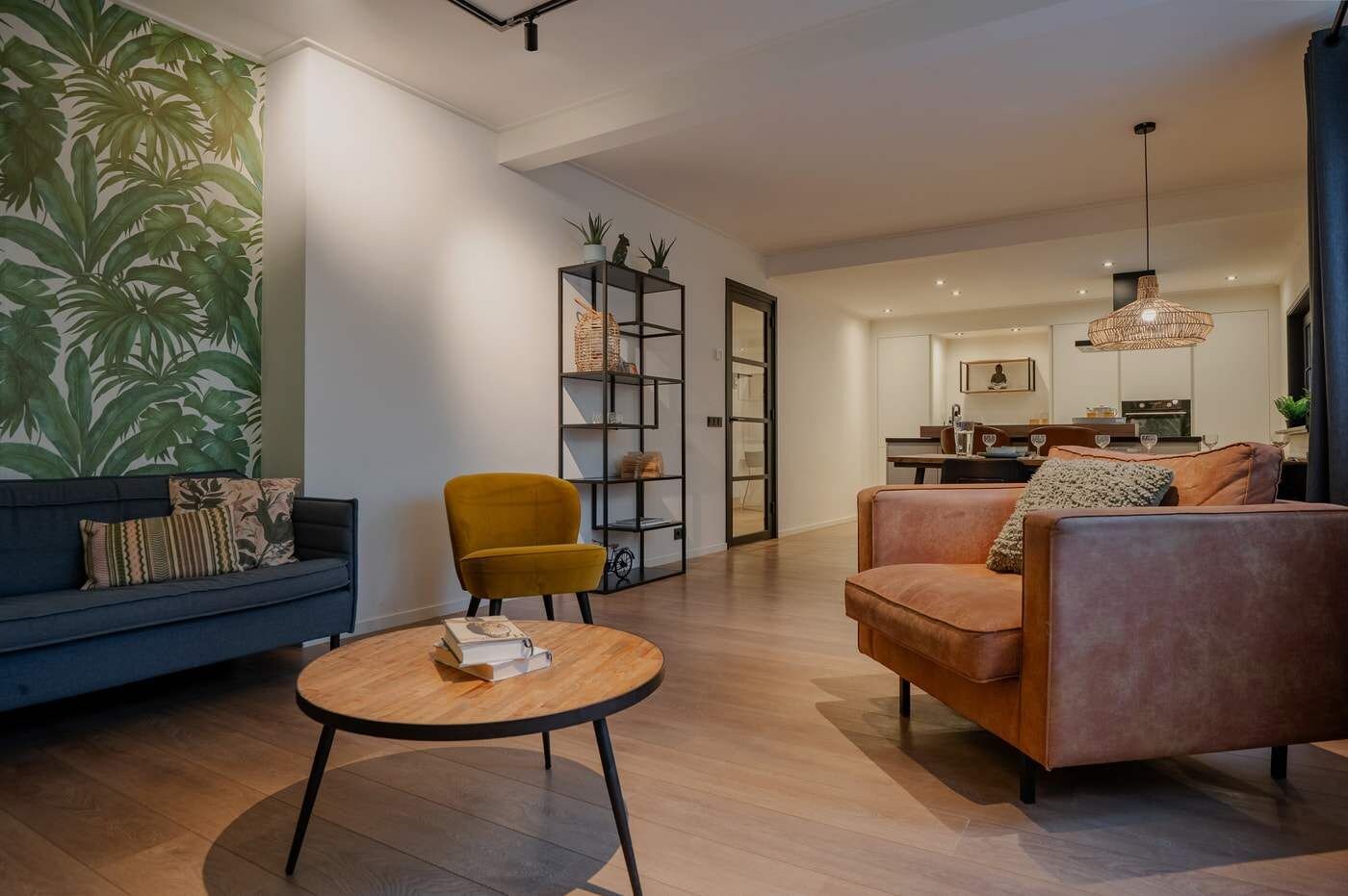 Een moderne woonkamer met een bank, fauteuil, bijzettafeltje en een boekenkast.