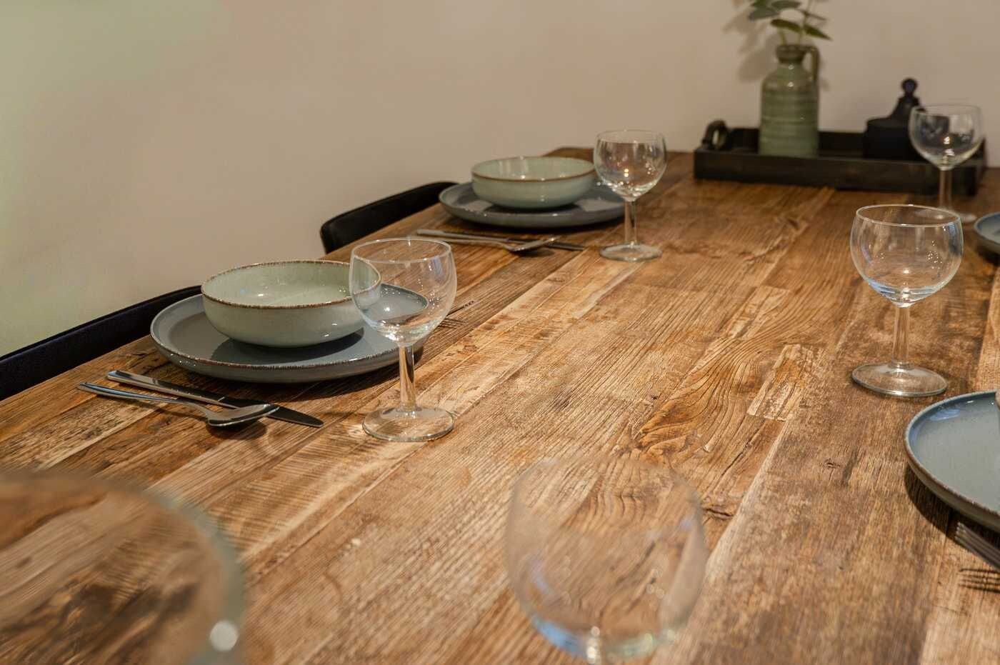 A wooden dining table with plates, bowls, and wine glasses set for a meal.