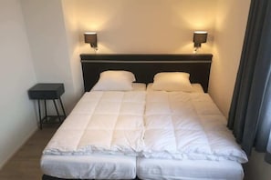 Ein Doppelbett mit zwei Nachttischlampen, einem kleinen Nachttisch und einem dunklen Kopfteil.