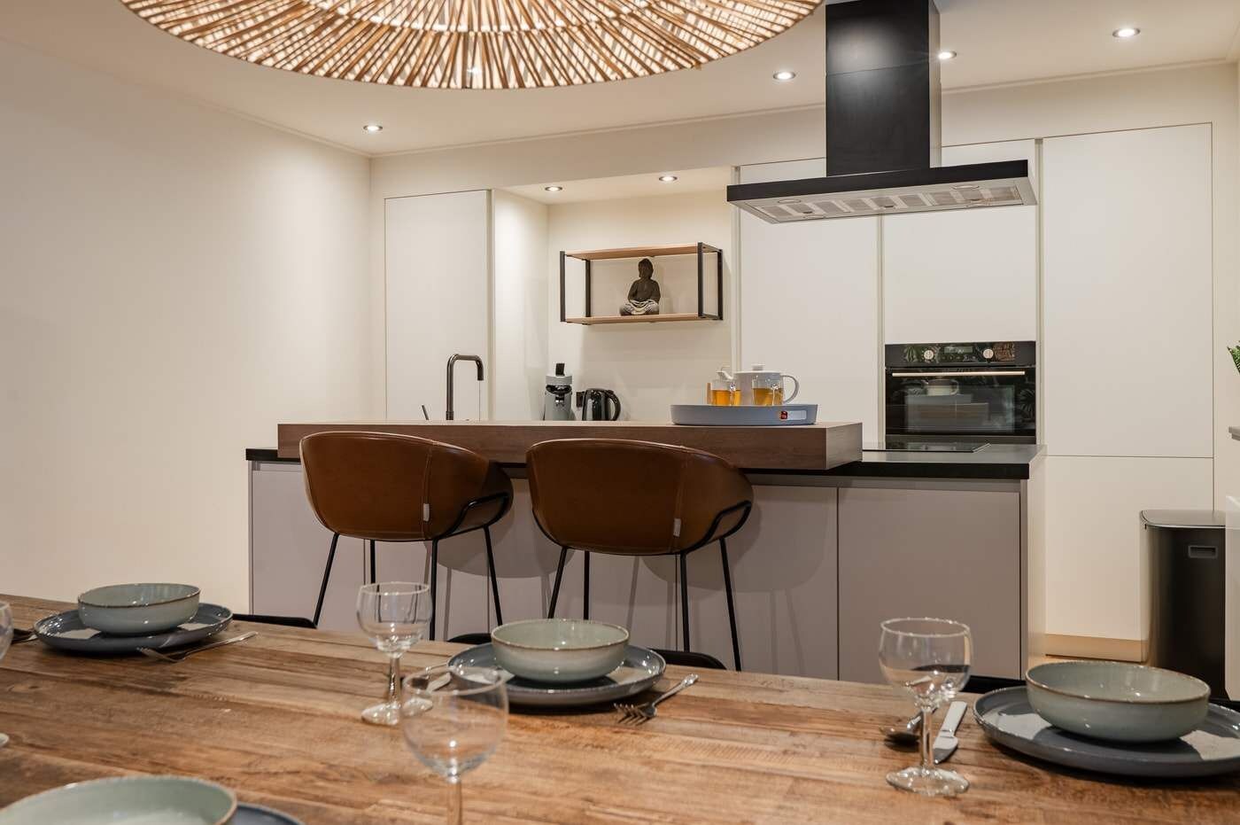 A modern kitchen with a central island, two brown chairs, and a dining table set with plates and glasses.