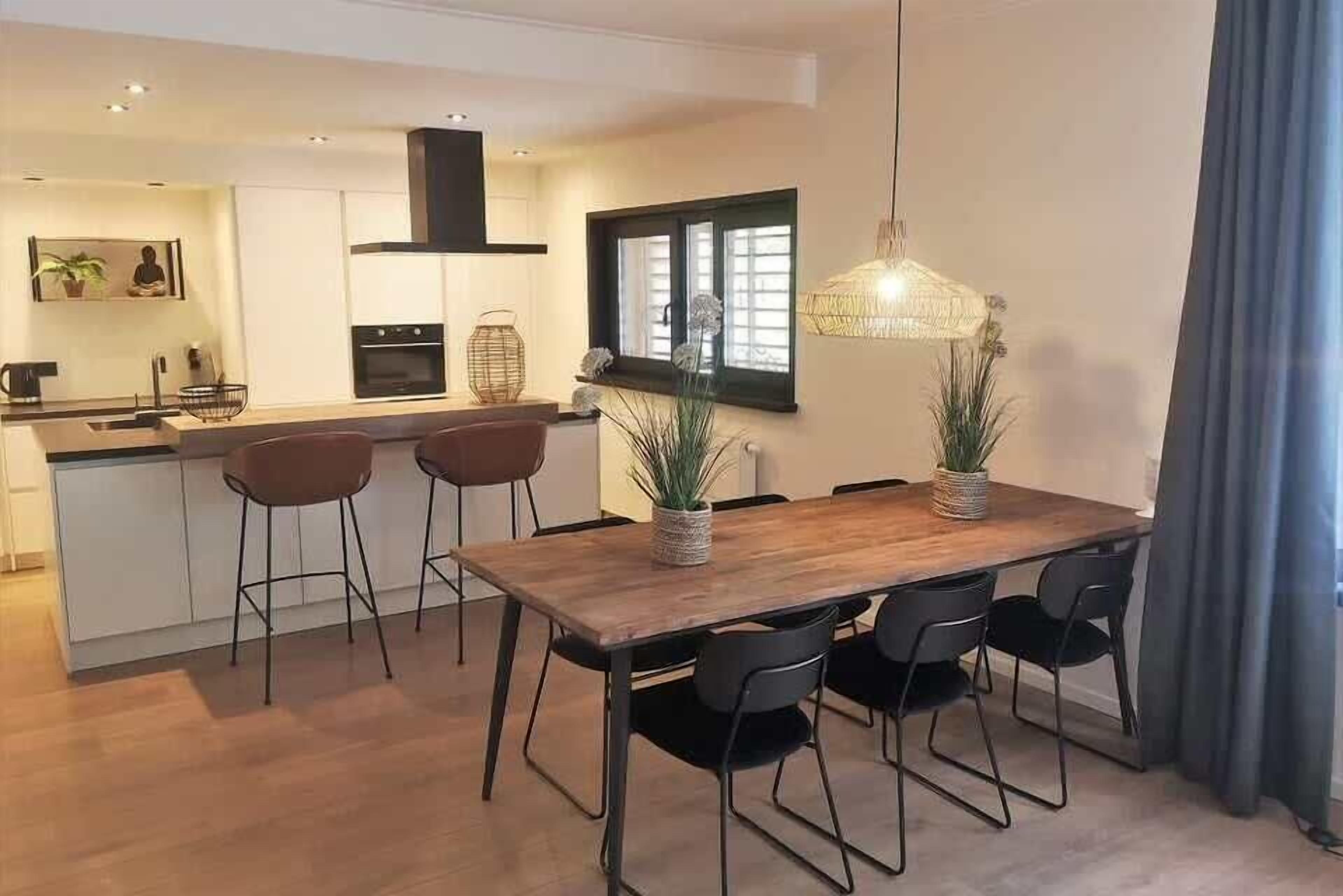 Eine moderne Küche mit Essbereich, ausgestattet mit einem Holztisch, schwarzen Stühlen und einer hängenden Leuchte.