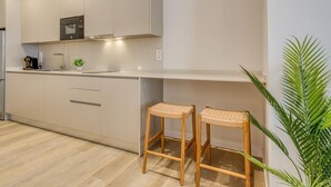 A modern kitchen with white cabinets, a built-in oven, and a coffee machine. There are two wooden stools with woven seats. - Modern studio near marina - 2 guests (Estepona)