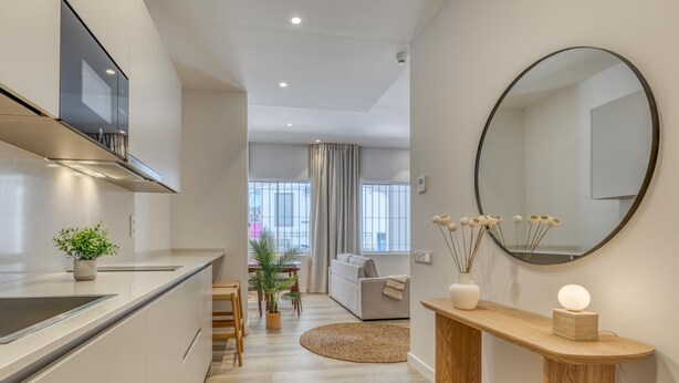 A modern kitchen with a built-in oven, a dining area with a round table and chairs, a living room with a sofa, and a round mirror on the wall. - Modern studio near marina - 2 guests (Estepona)