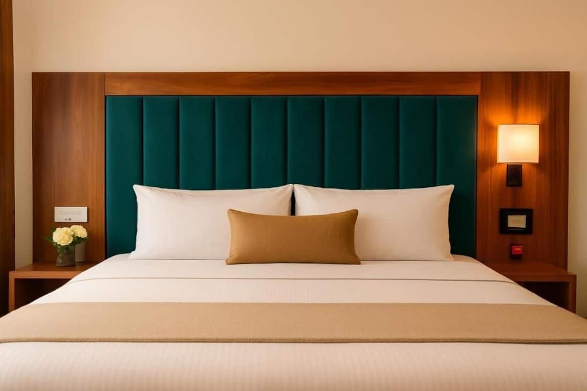 Una habitación de hotel con una cama, una mesita de noche con lámpara y un florero con flores.